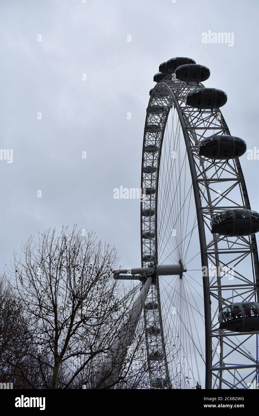 Das London Eye. Ein riesiges Beobachtungsrad auf dem Südufer. Ein Teil des Rades wird an einem wolkigen Wintertag mit Bäumen um den Rand des Bildes gezeigt. Stockfoto