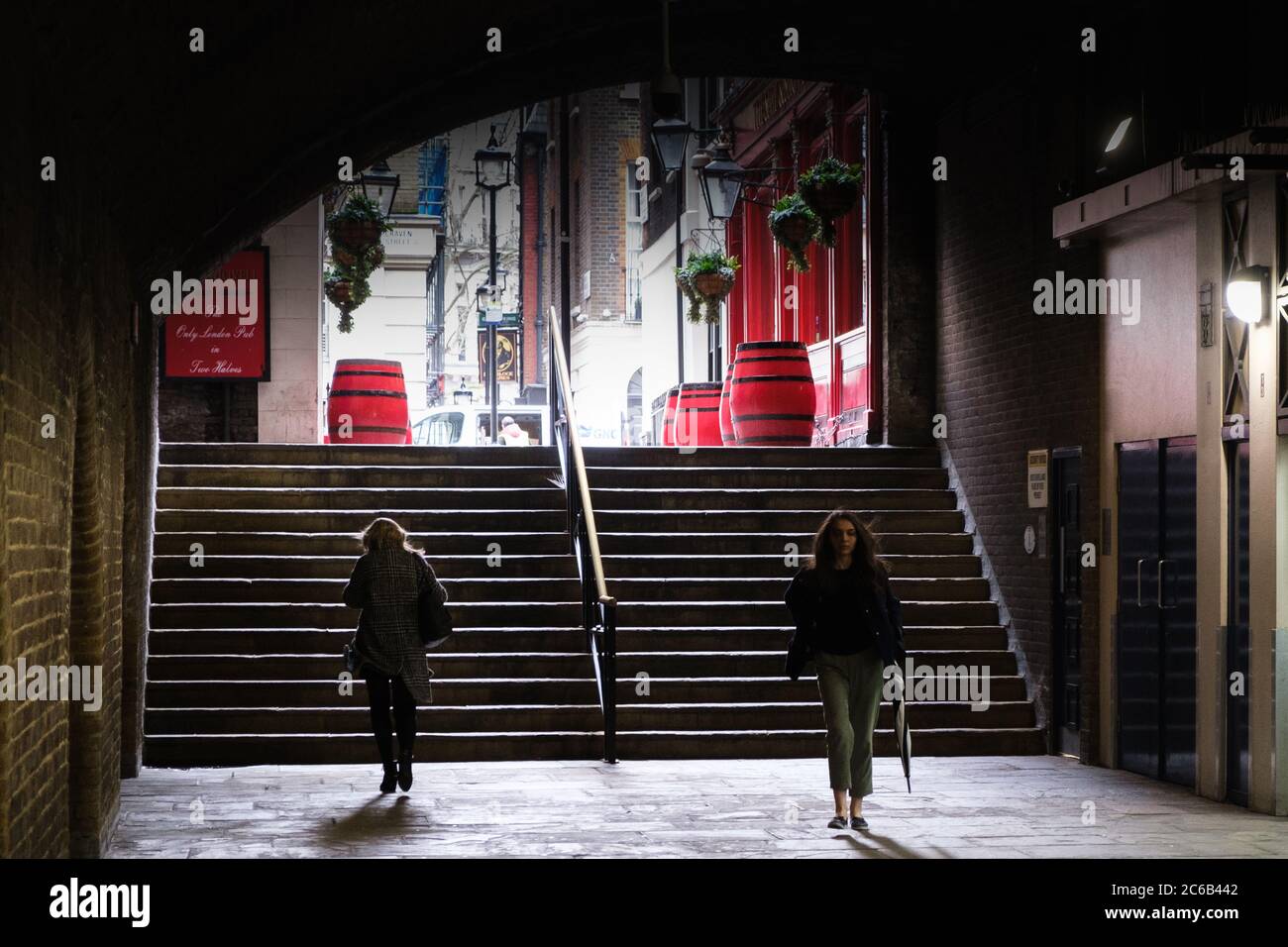 Zwei Damen passieren am unteren Ende der Treppe in einer moodily beleuchteten unterirdischen Einkaufsstraße in der Nähe der Embankment U-Bahnstation im Zentrum von London Stockfoto