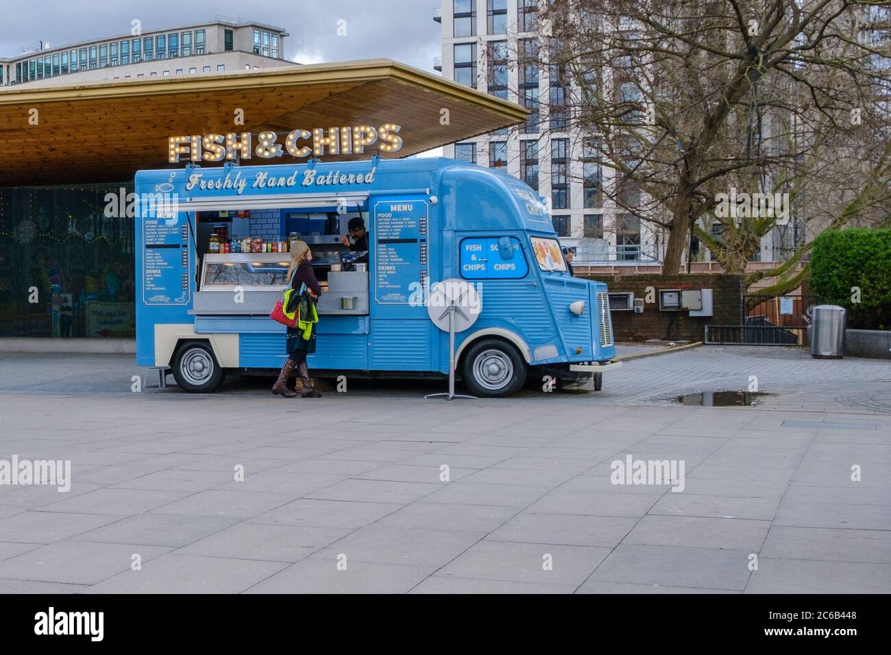 Niedlicher Retro-Van mit blauen Fischen und Chips, der auf Londons Southbank geparkt wurde. Einsame Kundin, die Lebensmittel kauft. Stockfoto