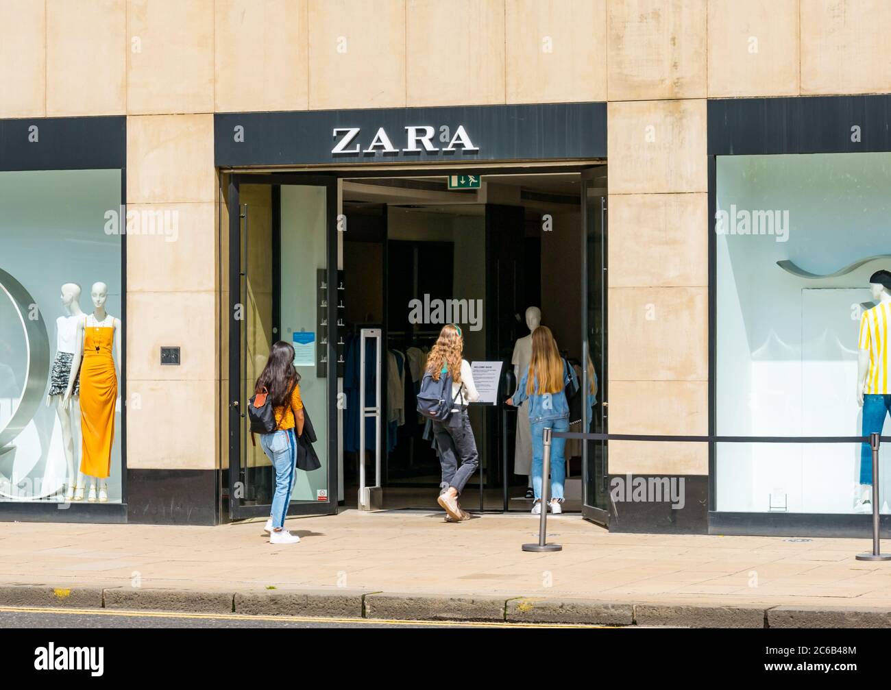 Mädchen betreten das Bekleidungsgeschäft Zara, nachdem sie die Handdesinfektionsmittel an der Tür, Princes Street, Edinburgh, Schottland, Großbritannien, lockert haben Stockfoto