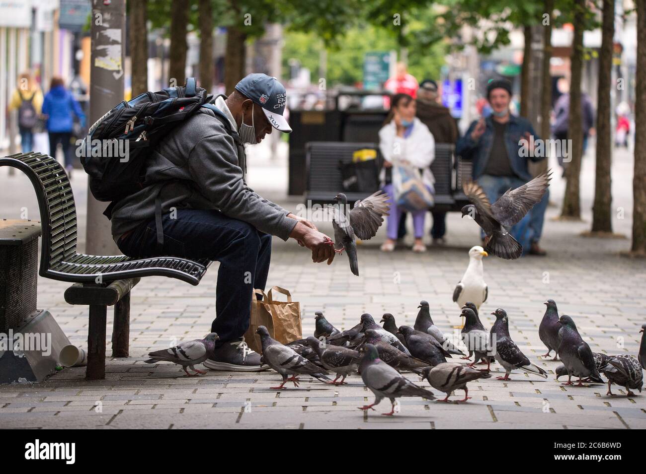 Glasgow, Schottland, Großbritannien. Juli 2020. Im Bild: Ein Mann füttert Tauben von Hand in der Sauchielhall Straße im Glasgows Einkaufsviertel. Quelle: Colin Fisher/Alamy Live News Stockfoto
