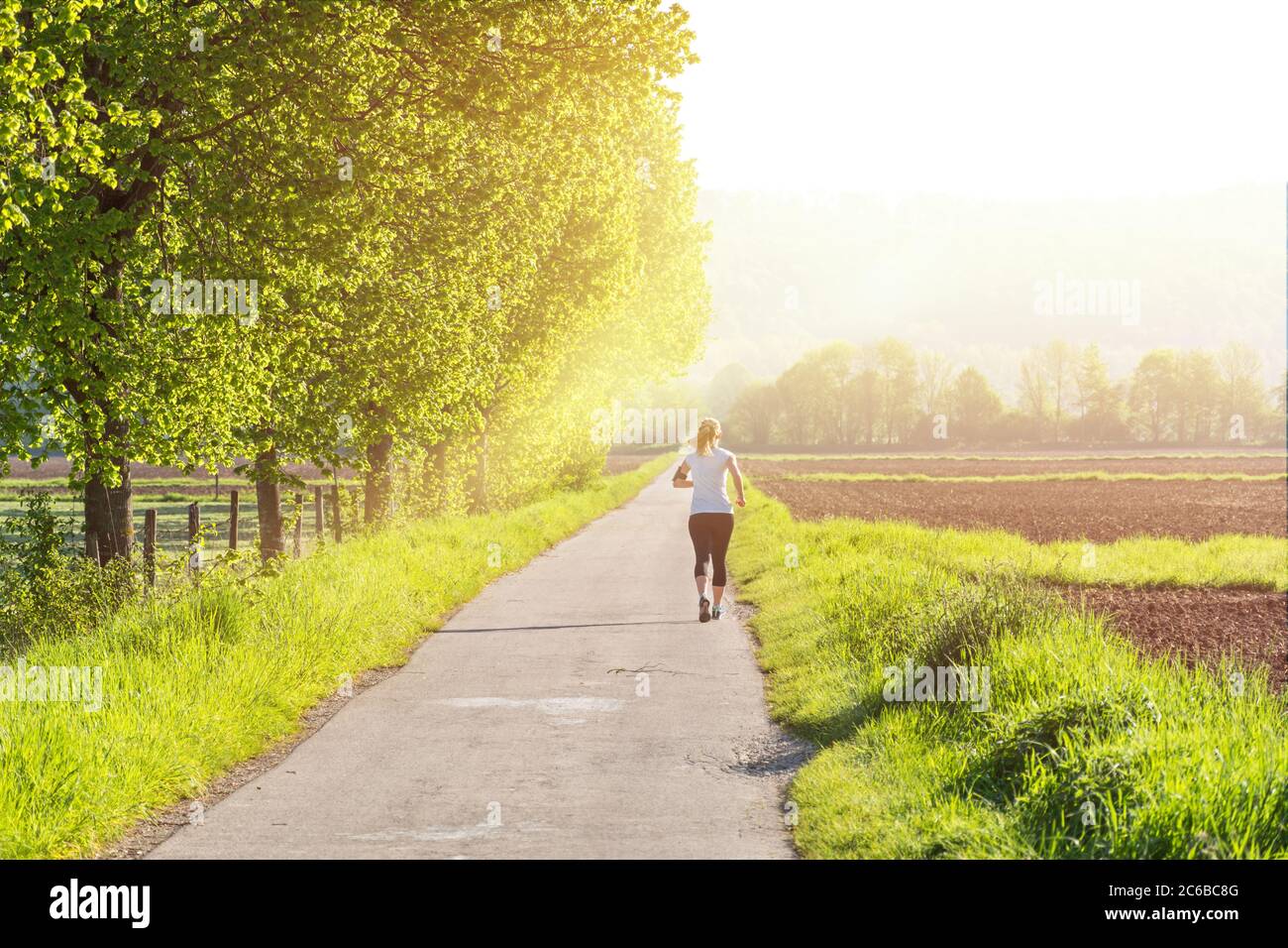 Joggingin auf einer Landstraße, die in Richtung aufgehender Sonne läuft Stockfoto