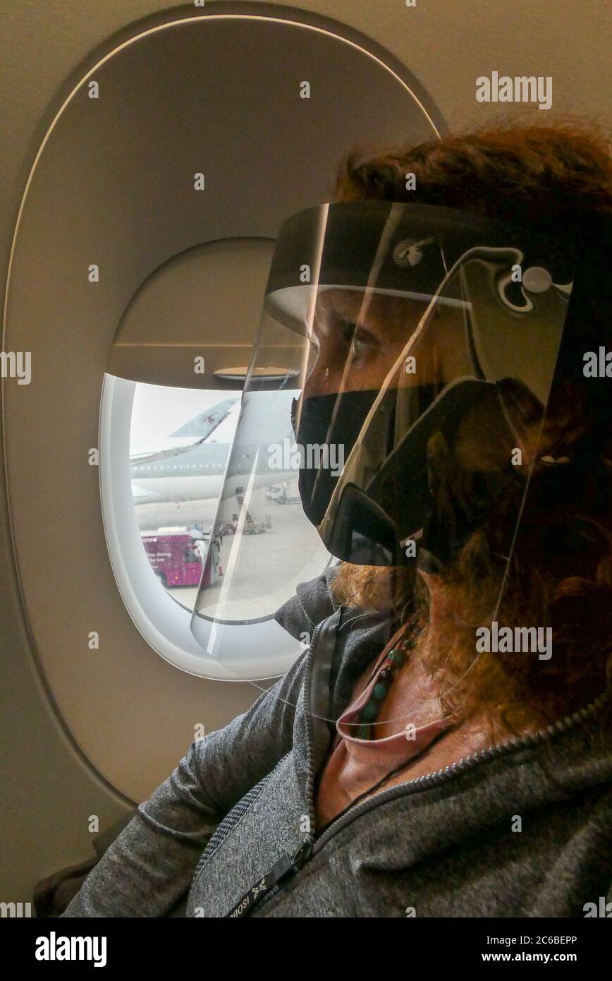 Passagier in einem Flugzeug, das nach 5 Monaten auf den Rückflug nach Großbritannien wartet, da Covid 19 PSA, Gesichtsmaske und Visierschutz trägt Stockfoto