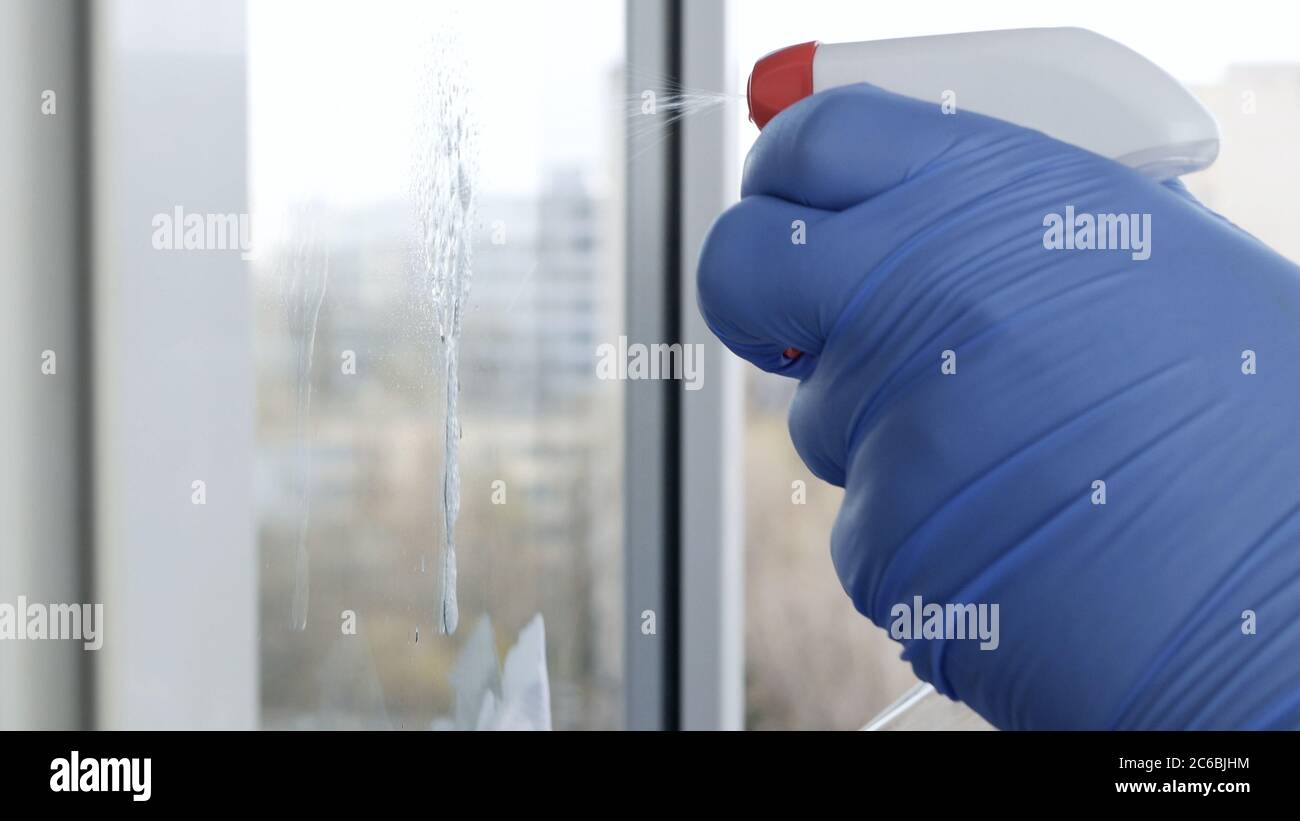 Nahaufnahme man Hände mit Schutzhandschuhe Reinigung eines Fensters mit gespritzten Flüssigkeit Desinfektion gegen Viren Kontamination Stockfoto