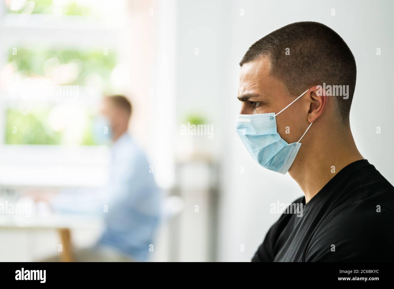 Junge Männliche Arbeiter Im Büro Trägt Medizinische Gesichtsmaske Stockfoto