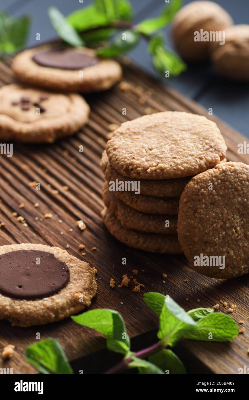 Gesunde zuckerfreie glutenfreie vegetarische Süßigkeiten. Erdnussbutter-Kekse mit dunklen Schokoladentropfen serviert mit roher Minze auf dunklem Eichenbrett Hintergrund Stockfoto