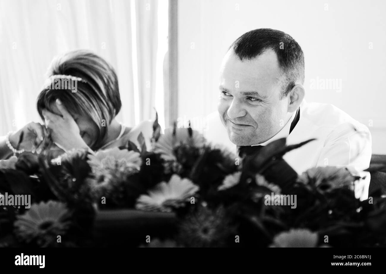 Braut Facepalms während Bräutigam in seinen vierziger Jahren peinlich lacht während Hochzeit besten Mann Rede. Ehrliche Reportage echt uninszenierte Facepalm witziger Moment. Stockfoto