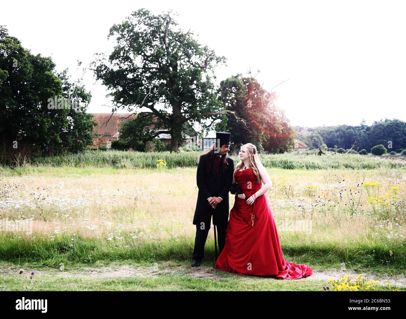 Bräutigam Dreißiger & Braut Zwanziger in Gothic Hochzeitsmode mit rotem Kleid, Gothic Zylinderhut, Schwänze & Stock. Stockfoto
