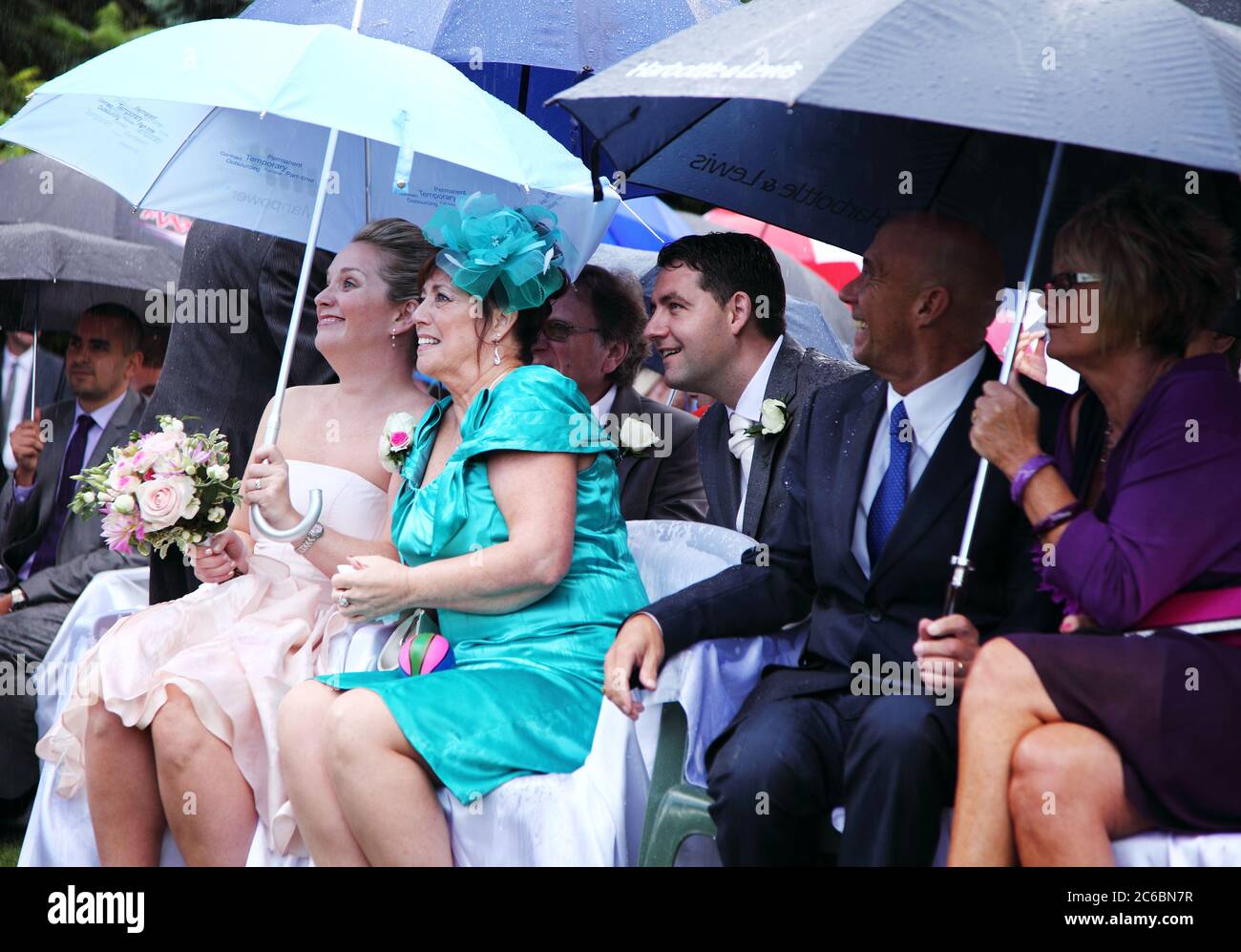 Hochzeitsgäste schützen sich bei einer Hochzeit im Freien unter Regenschirmen vor Regen. Stockfoto