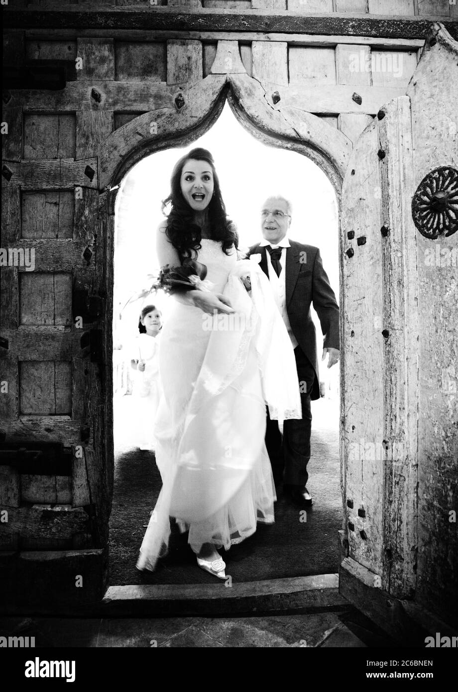 Aufgeregt, überrascht, Braut, dreißiger Jahre, und Vater der Braut, sechziger Jahre, zu Fuß durch eine alte Tür in die Trauung am Hochzeitstag Stockfoto