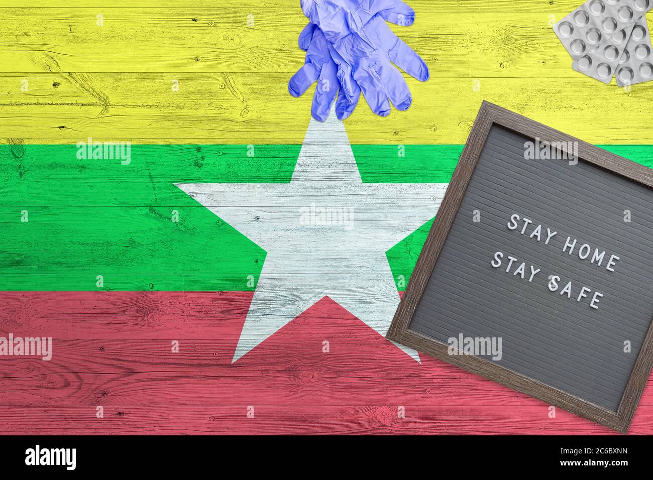 Myanmar Flagge Hintergrund auf Holztisch. Stay Home Schreibtafel, OP-Handschuhe, Pillen mit minimalem nationalen Covid 19 Konzept. Stockfoto