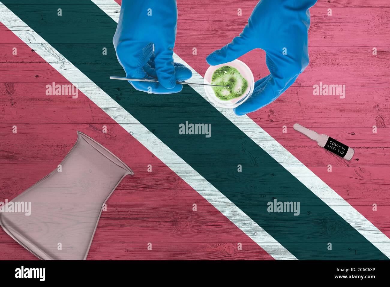 Trinidad und Tobago Flagge auf Labortisch. Medizinischer Techniker mit COVID-19-Abstrichbesteck, blaue Schutzhandschuhe, ep Stockfoto