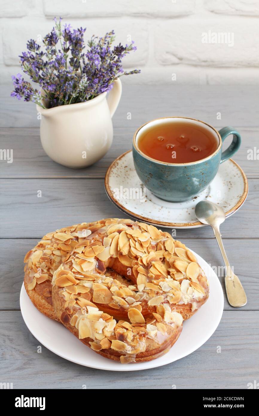 Brezeln mit gehackten Mandeln und einer Tasse Kräutertee auf einem grauen Holztisch bestreut. Nahaufnahme Stockfoto