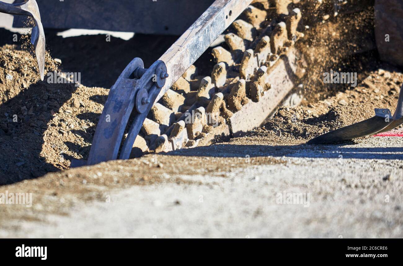 Nahaufnahme einer Grabenschaufelkette in Bewegung Graben einen Graben in Schmutz mit Arbeitern schaufeln zur Seite Stockfoto