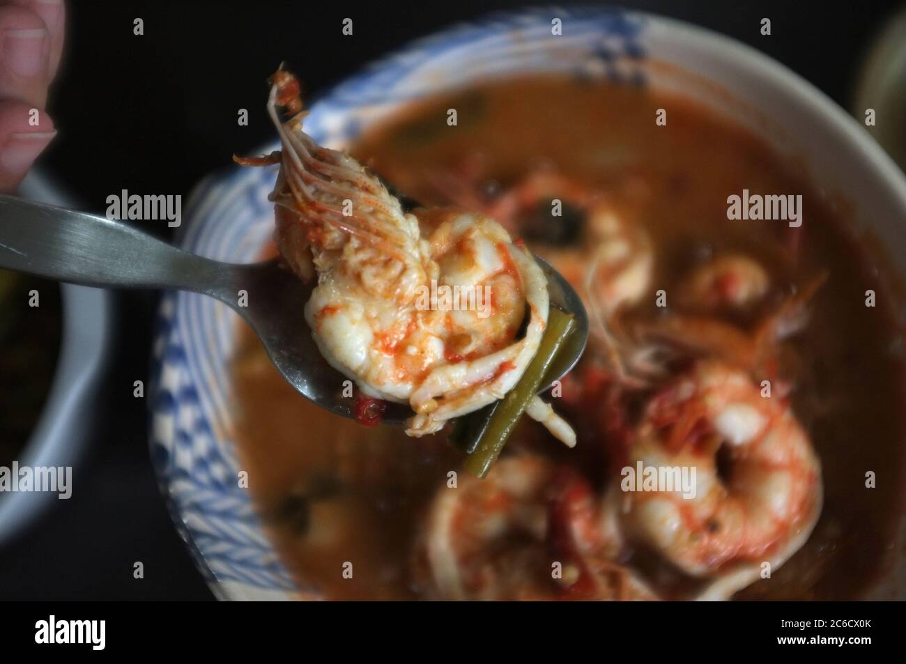 Close up Frau Hand halten einen Löffel mit Garnelen von Tom Yum Goong Spicy Sour Soup oder River Garnelen würzige Suppe auf Holztisch . Thai-Essen Stockfoto