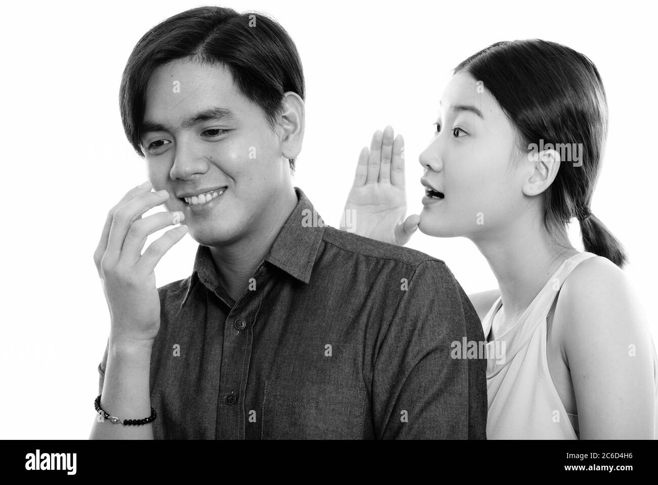 Studio-Aufnahme von jungen glücklich asiatischen Paar lächelnd mit Frau flüsternd Mann Stockfoto