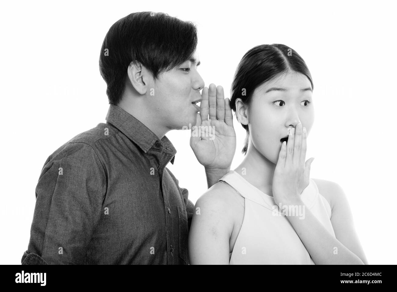 Studio-Aufnahme von jungen asiatischen Paar mit Mann flüsternd zu Frau suchen schockiert Stockfoto