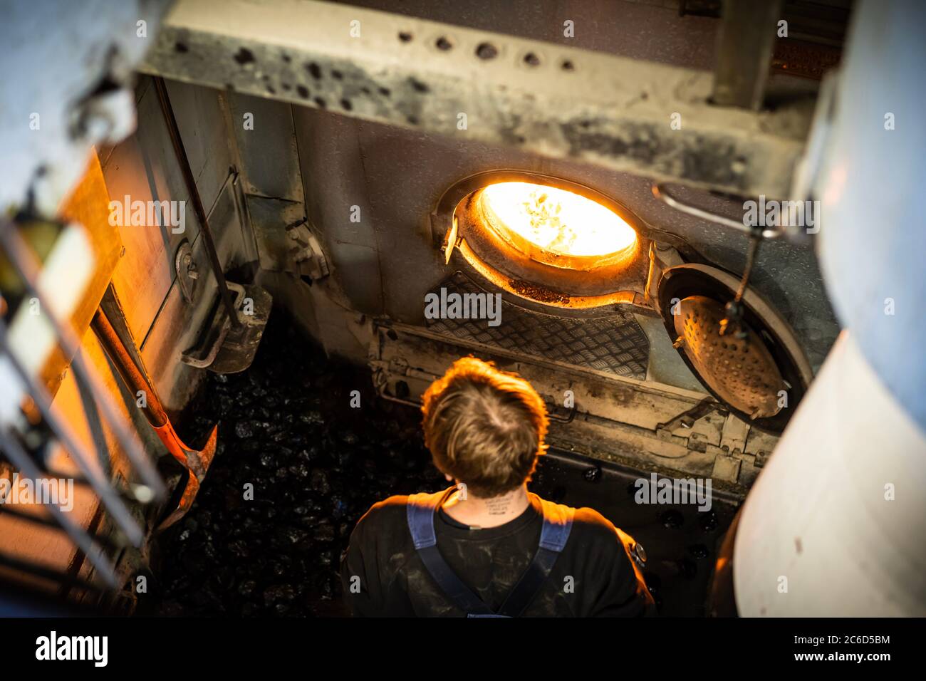 Ein Arbeiter fügt eine Kohle in den Motor des Dampfschiffs mit gecoaled Kraft ein Stockfoto
