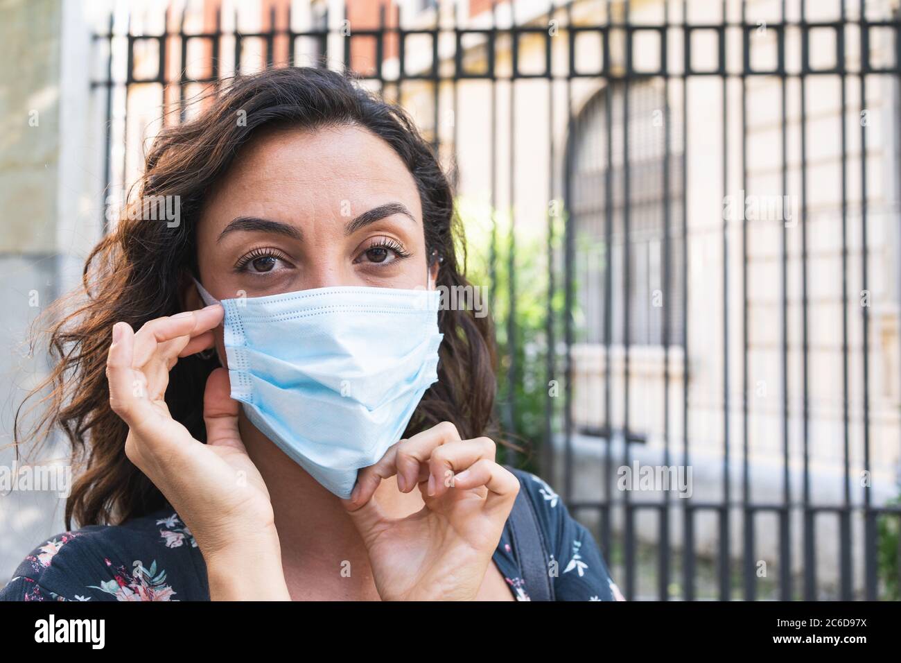 Junge Frau, die auf der Straße eine chirurgische Maske aufsetzt, um sich zu schützen und hygienische Sicherheitsmaßnahmen zu treffen. Konzept von Schutz und Sicherheit Stockfoto