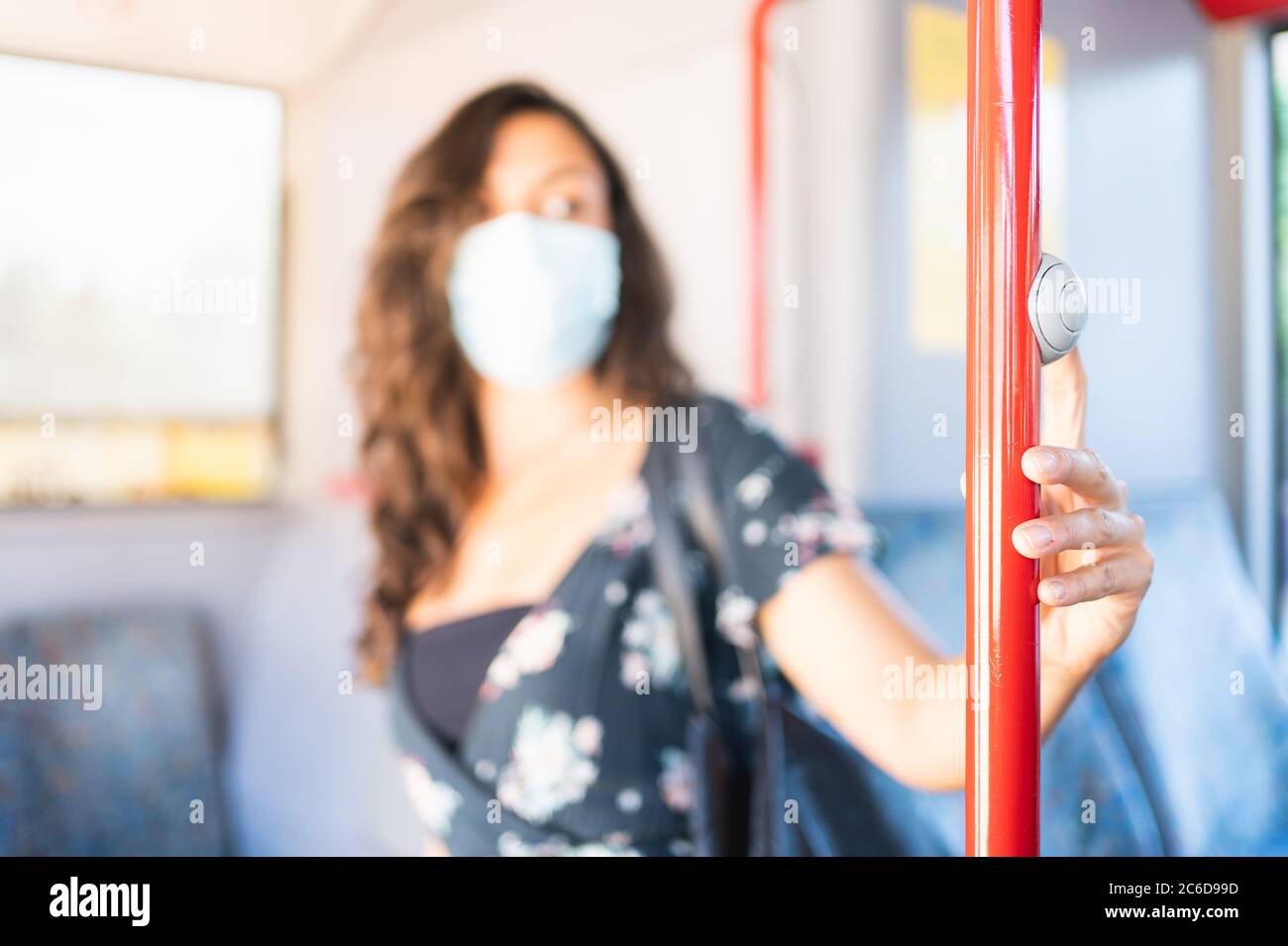 Junge Frau, die den Fahrer mit einer Schutzmaske ansieht und den Stoppknopf berührt, um aus dem Bus auszusteigen. Schutzkonzept Stockfoto