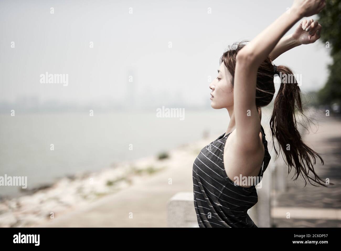 Junge asiatische Erwachsene Frau Stretching Arme im Freien am Meer, Seitenansicht Stockfoto