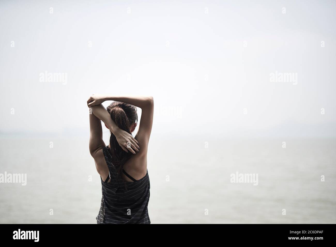 Junge asiatische Erwachsene Frau dehnt Arme im Freien am Meer, Rückansicht Stockfoto