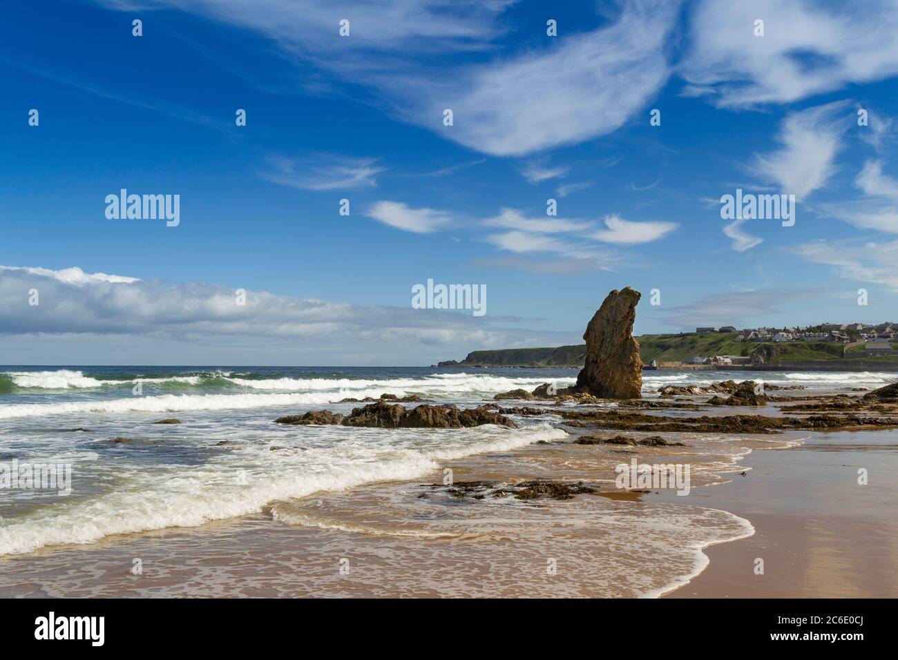 CULLEN BAY BEACH UND STADT MORAY COAST SCOTLAND EIN BLAUER HIMMEL UND EIN SANDSTRAND MIT WELLEN, DIE AUF DEN MEERESSTAPEL BRECHEN Stockfoto