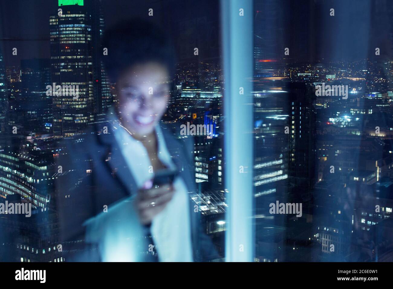 Lächelnde Geschäftsfrau, die im Stadtfenster das Handy überprüft Stockfoto