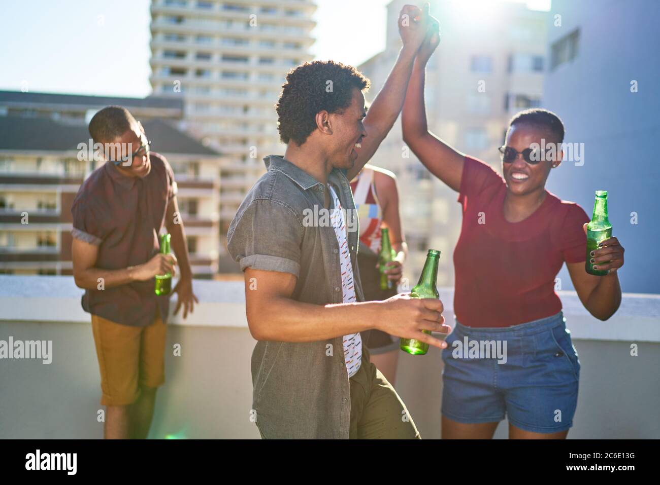 Fröhliche junge Freunde, die auf dem sonnigen städtischen Dach tanzen und Bier trinken Stockfoto
