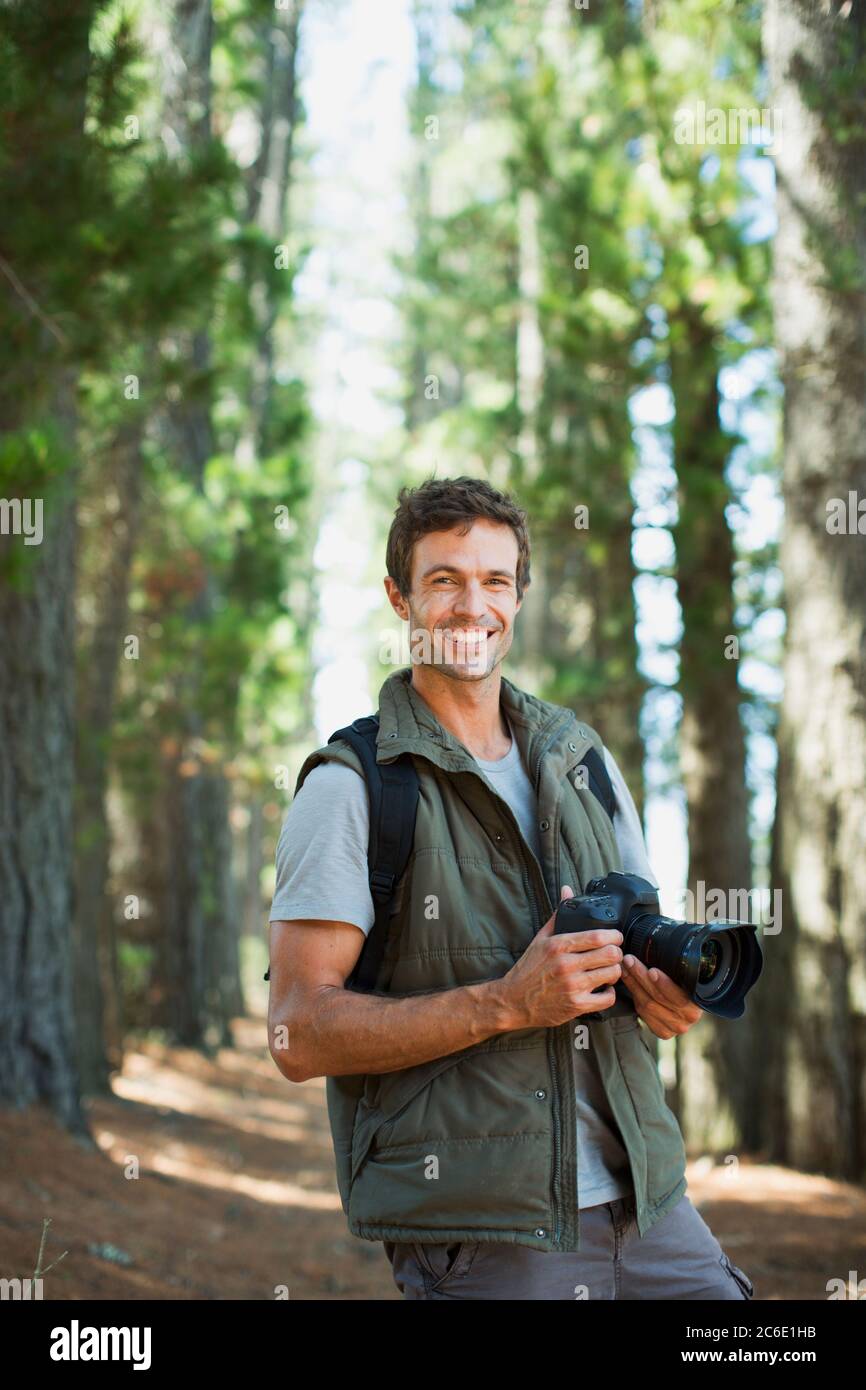 Lächelnder Mann mit Digitalkamera im Wald Stockfoto
