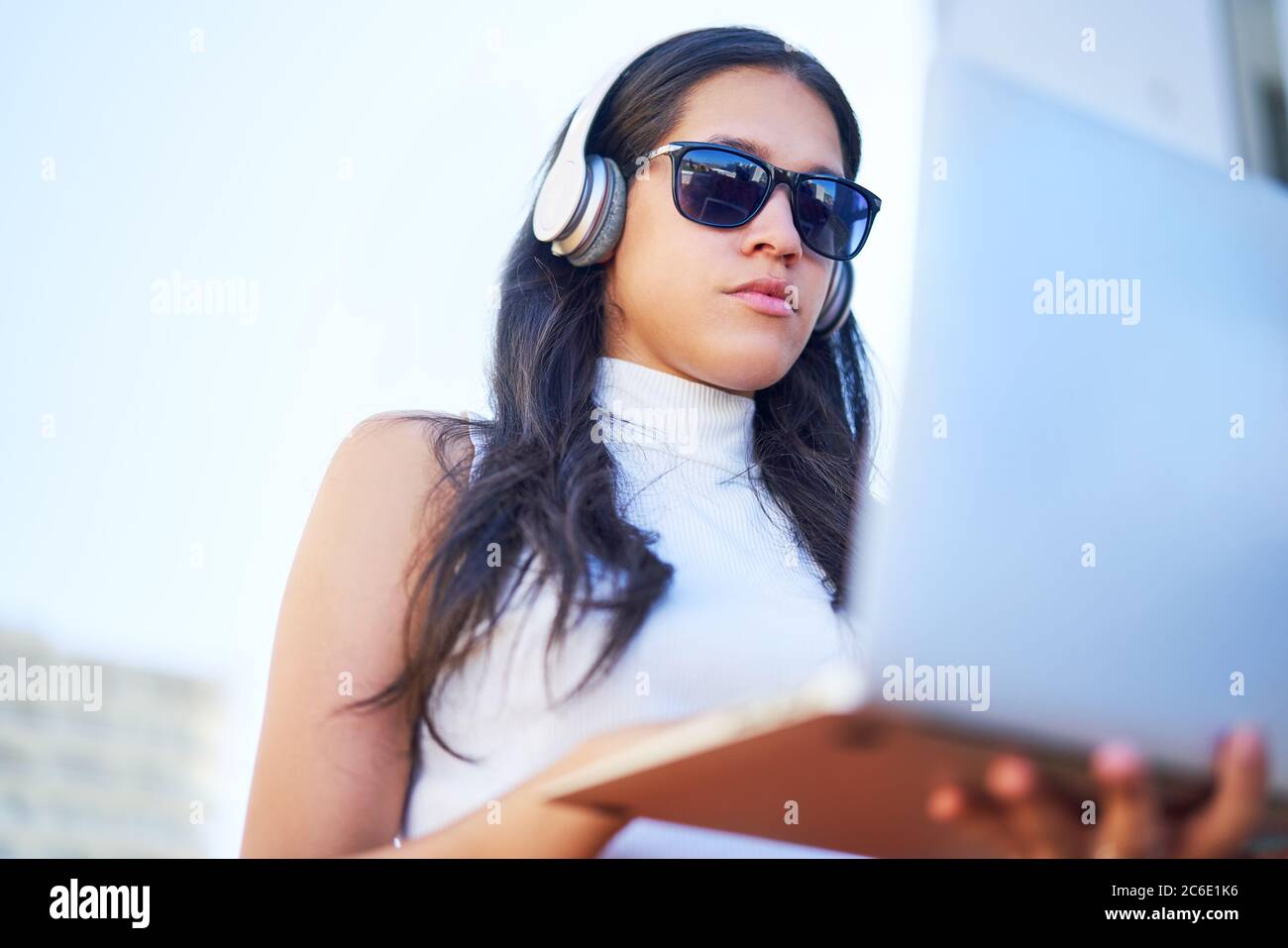Junge Frau mit Kopfhörer und Sonnenbrille mit Laptop Stockfoto