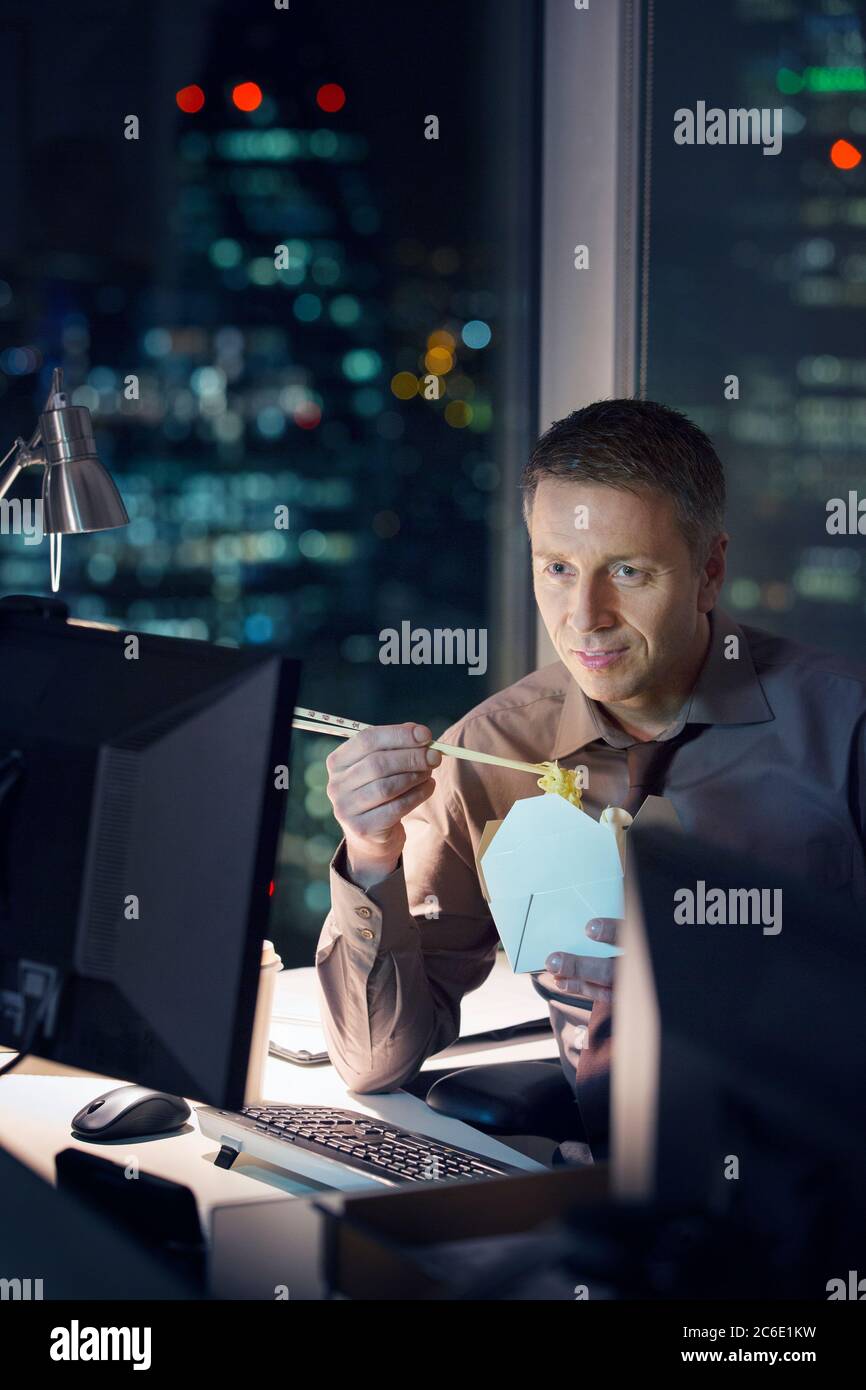 Geschäftsmann, der abends Essen zum Mitnehmen an der Rezeption im Büro isst Stockfoto