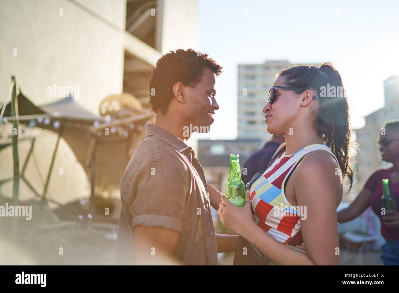 Glückliches junges Paar, das Bier trinkt und auf dem sonnigen städtischen Dach spricht Stockfoto