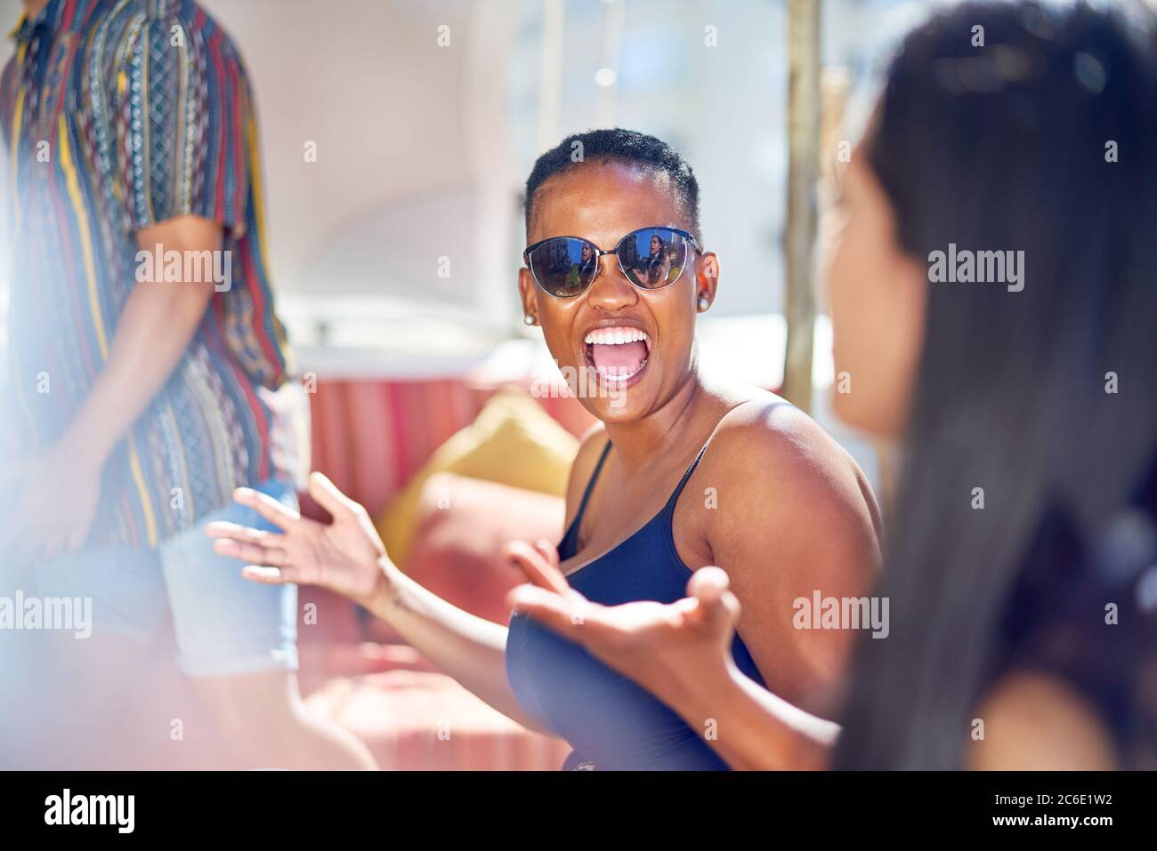 Glückliche junge Frau, die mit Freunden auf der sonnigen Terrasse lacht Stockfoto