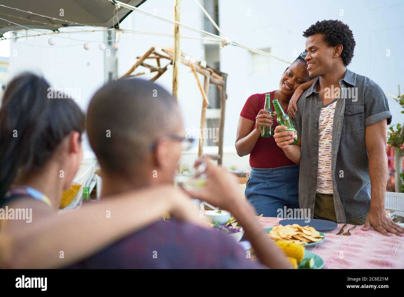 Glückliche junge Freunde, die Bier trinken und am Tisch auf der Terrasse essen Stockfoto