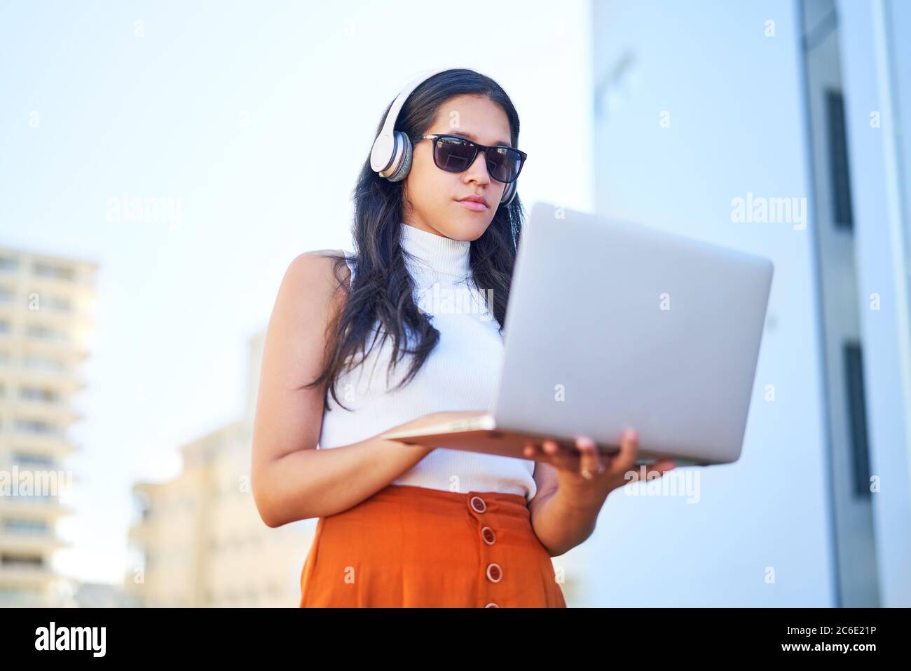 Junge Frau mit Kopfhörern mit Laptop auf städtischen Balkon Stockfoto