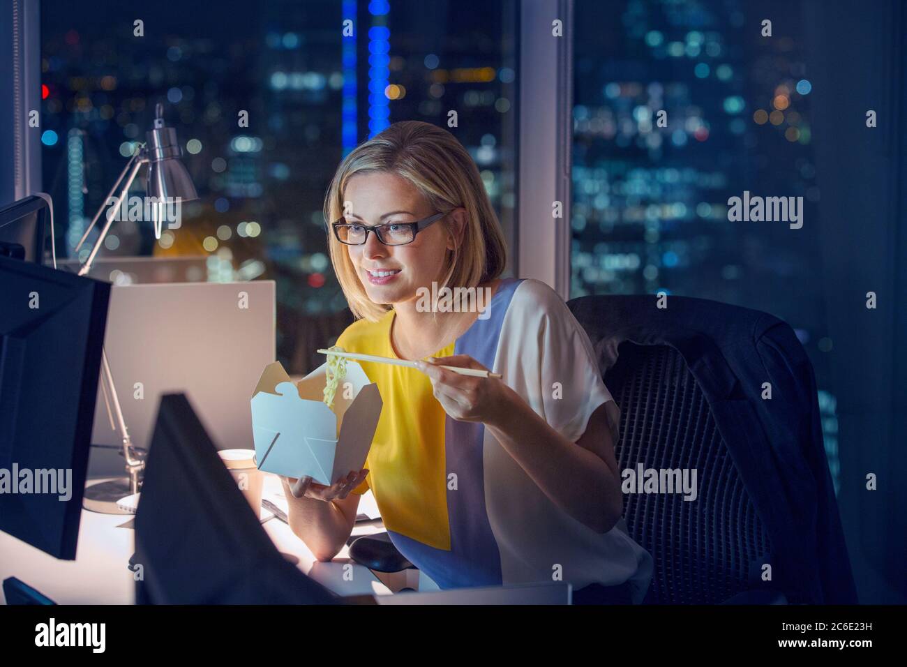 Geschäftsfrau, die abends Essen zum Mitnehmen an der Rezeption im Büro isst Stockfoto