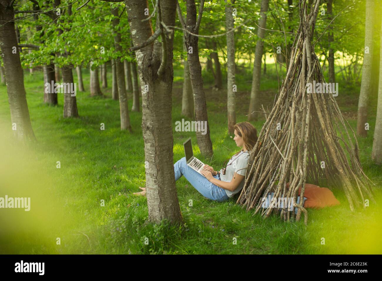 Frau mit Laptop entspannen an Zweig Tipi in Wäldern Stockfoto