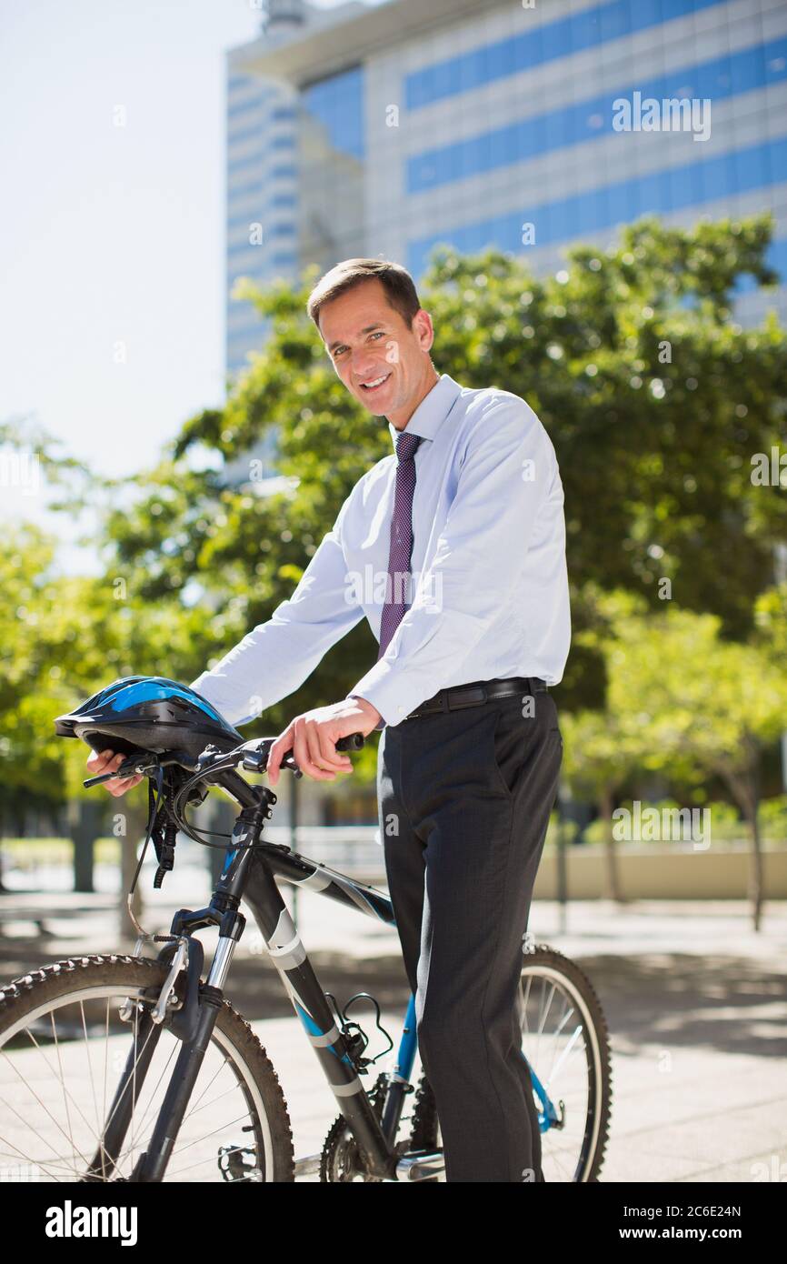 Lächelnder Geschäftsmann mit Fahrrad und Helm im Stadtpark Stockfoto