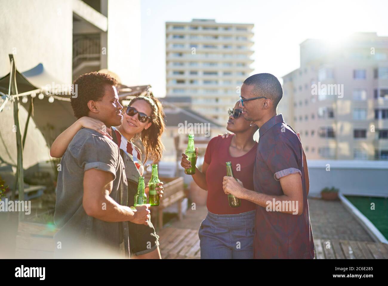 Junge Freunde trinken Bier auf dem sonnigen städtischen Dachbalkon Stockfoto