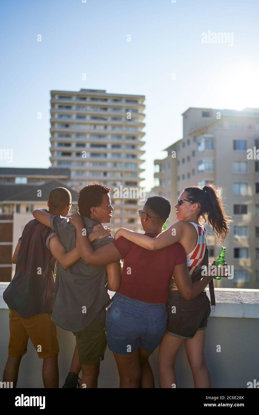 Glückliche junge Freunde, die auf dem sonnigen städtischen Dachbalkon hängen Stockfoto