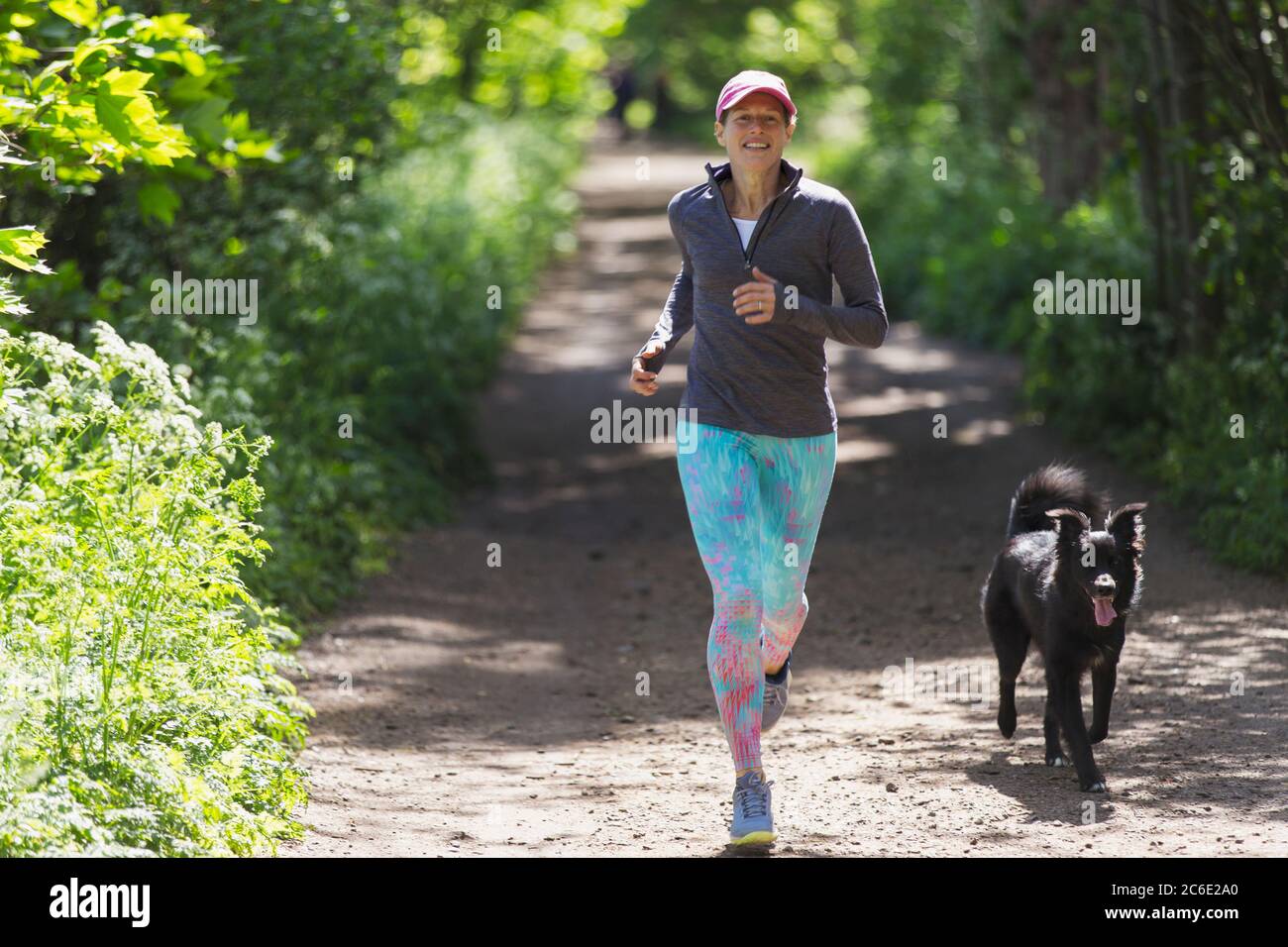 Frau joggt mit Hund auf sonnigem Trail Stockfoto