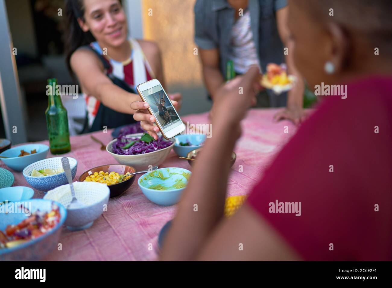 Junge Frau zeigt Smartphone an Freund auf Terrasse Tisch Stockfoto