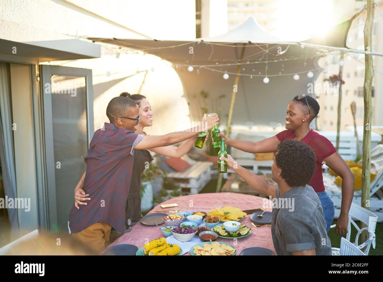 Fröhliche junge Freunde, die Bier über dem Tisch auf der Terrasse toasten Stockfoto