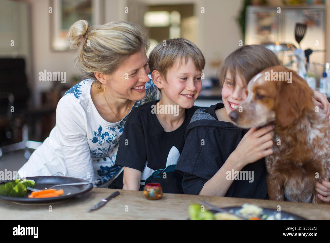 Glückliche Mutter und Söhne mit Hund am Esstisch Stockfoto