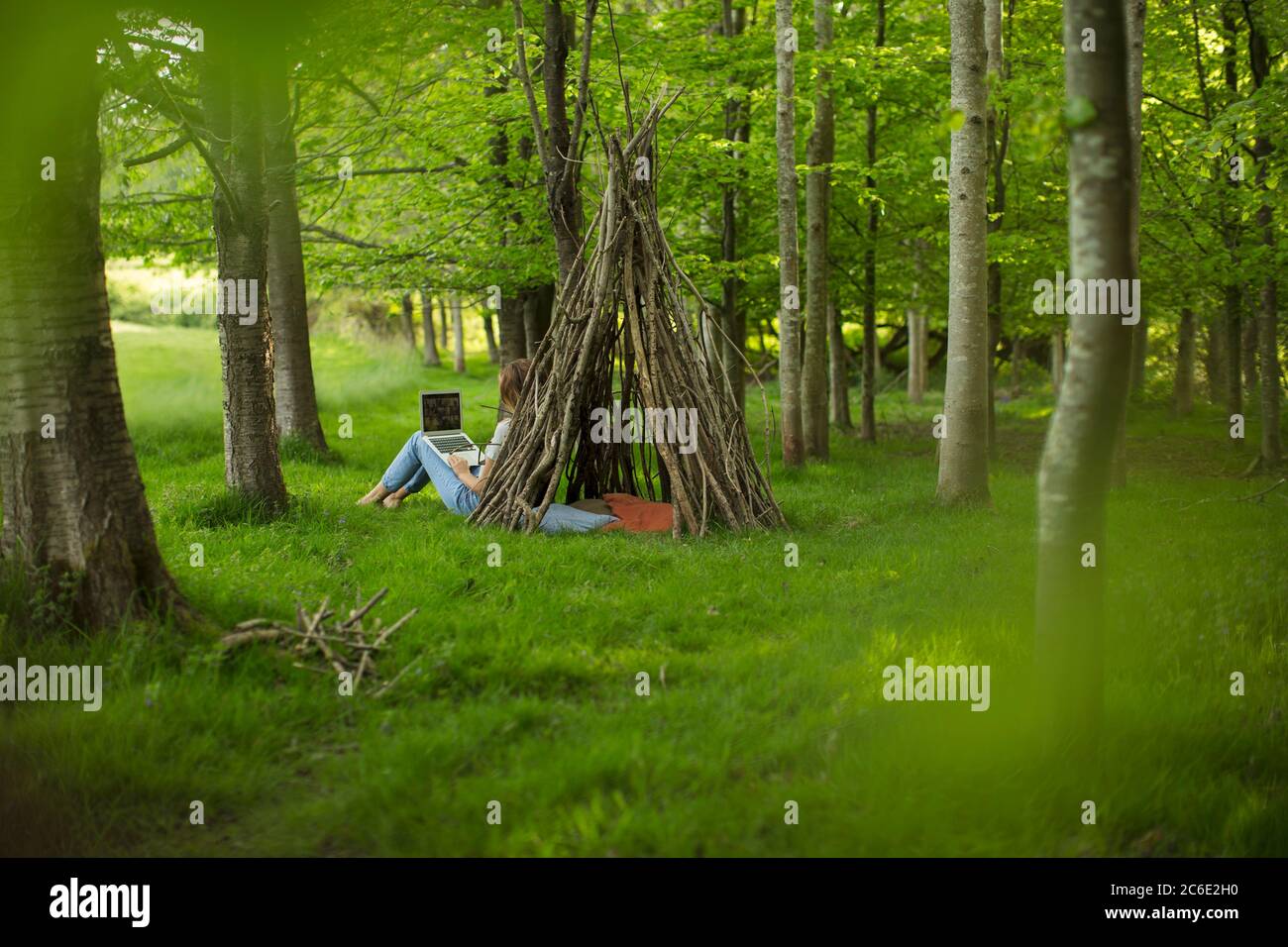 Junge Frau mit Laptop an Zweig Tipi im Wald Stockfoto
