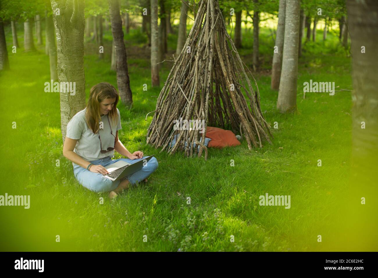 Junge Frau mit Laptop an Zweig Tipi in Wäldern Stockfoto
