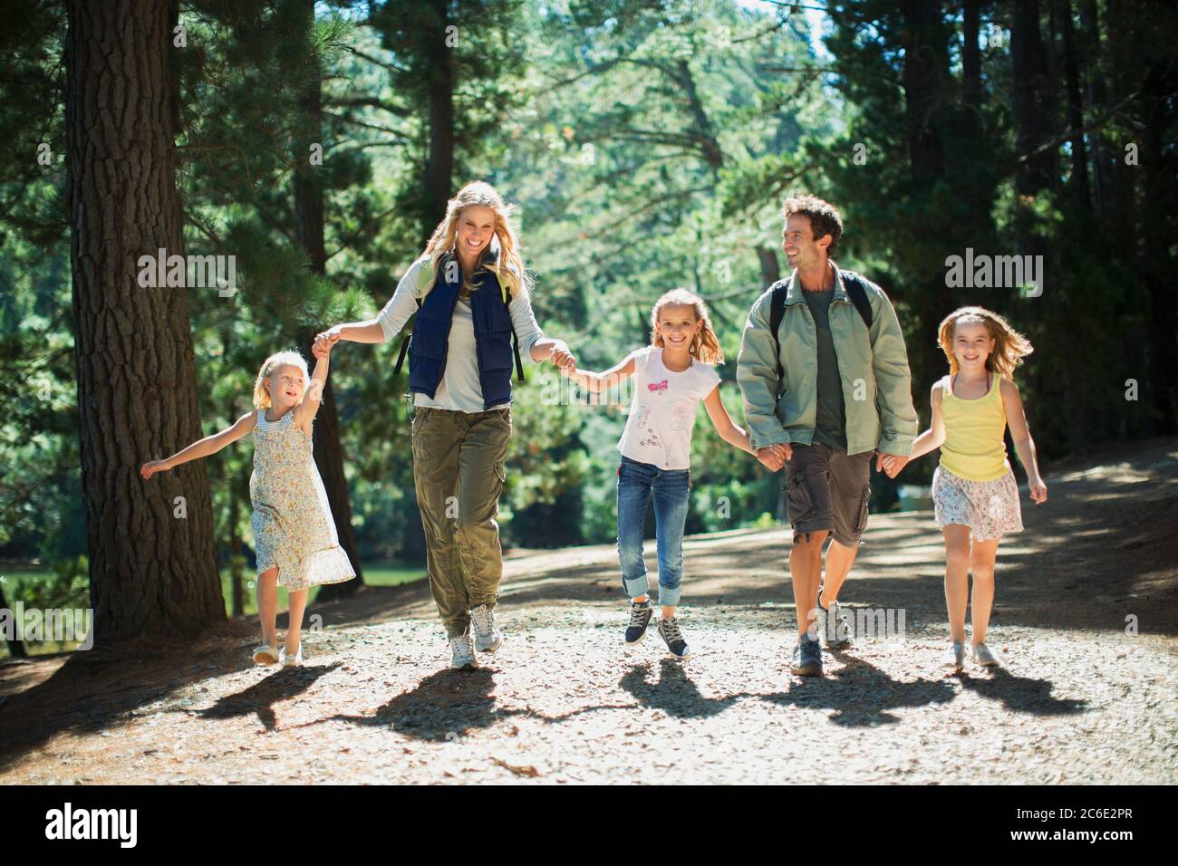 Lächelnde Familie, die Hände hält und im Wald läuft Stockfoto