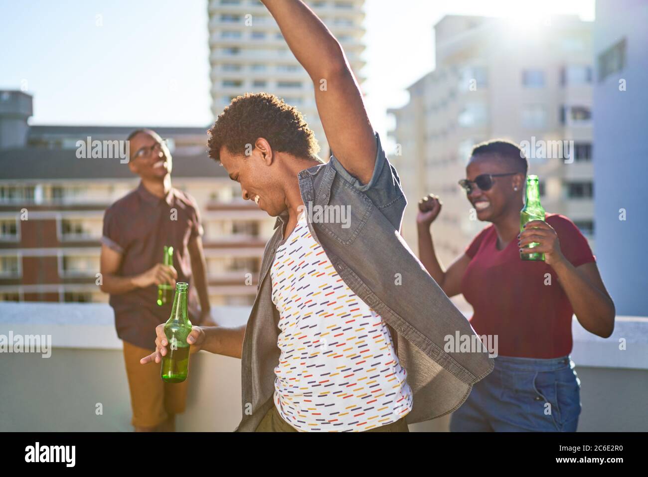 Unbeschwerte junge Freunde tanzen und trinken Bier auf der sonnigen Dachterrasse Stockfoto