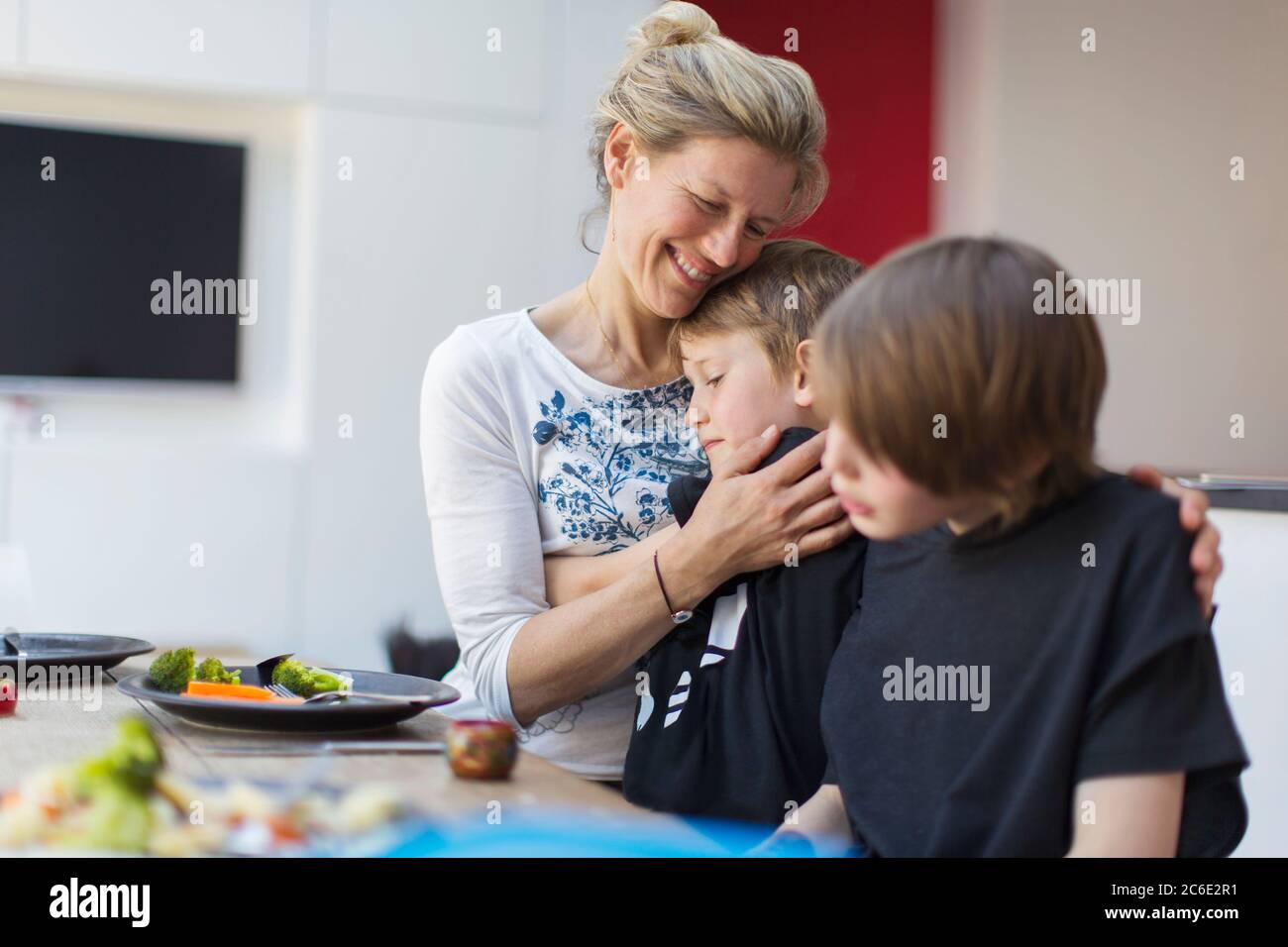 Liebevolle Mutter umarmt Söhne am Esstisch Stockfoto